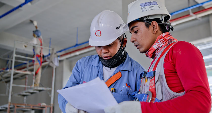 Two construction workers looking at a paper.