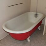 A red and white bathtub in the corner of a bathroom.