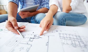 Two people are sitting at a table with plans on it.