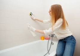 A woman in white shirt and gloves cleaning bathtub.