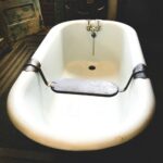 A white bathtub with black trim and a wooden bench.