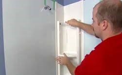 A man is putting the door on a bathroom wall.